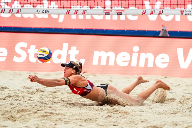 Eine Frau taucht in den Sand, um einen Volleyball zu fangen.