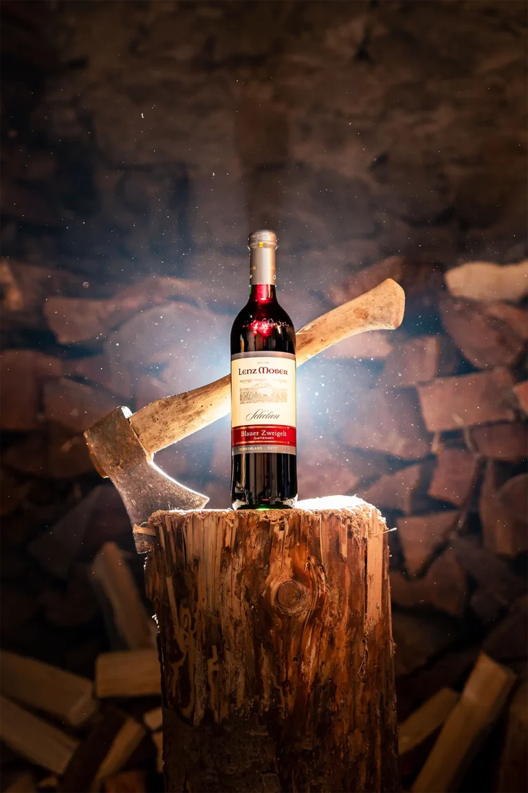 Eine Flasche Wein steht auf einem Baumstamm in einem dunklen Raum.